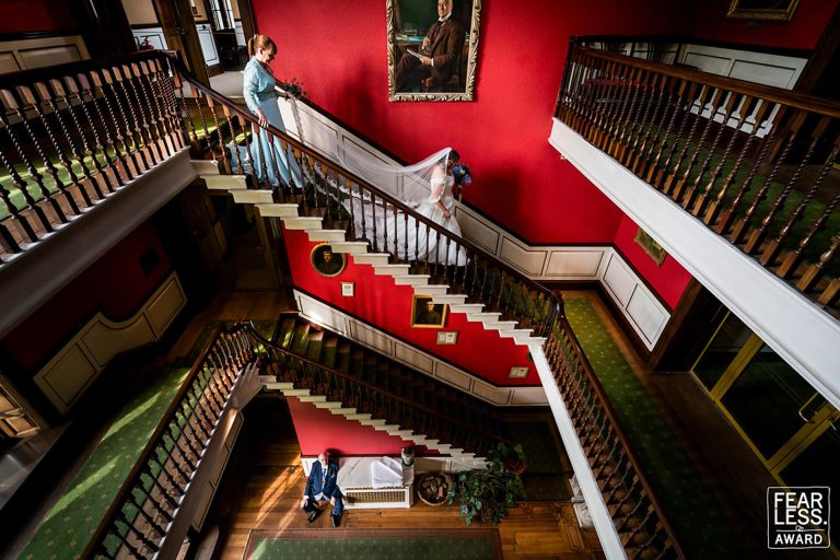 Bride descending ornate staircase in elegant red-walled mansion