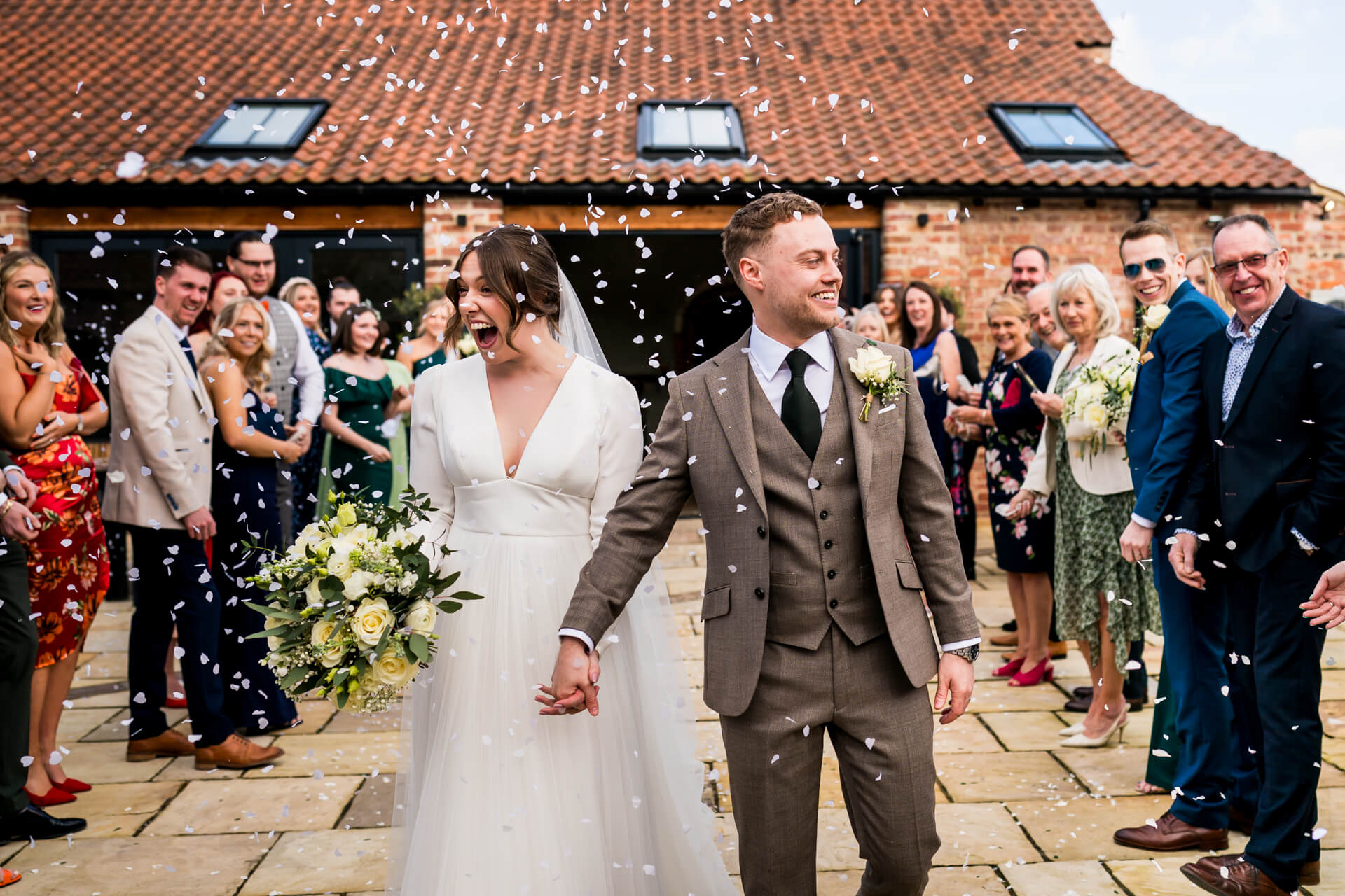 Joyful wedding couple with confetti and cheering guests at Thirsk Lodge barns