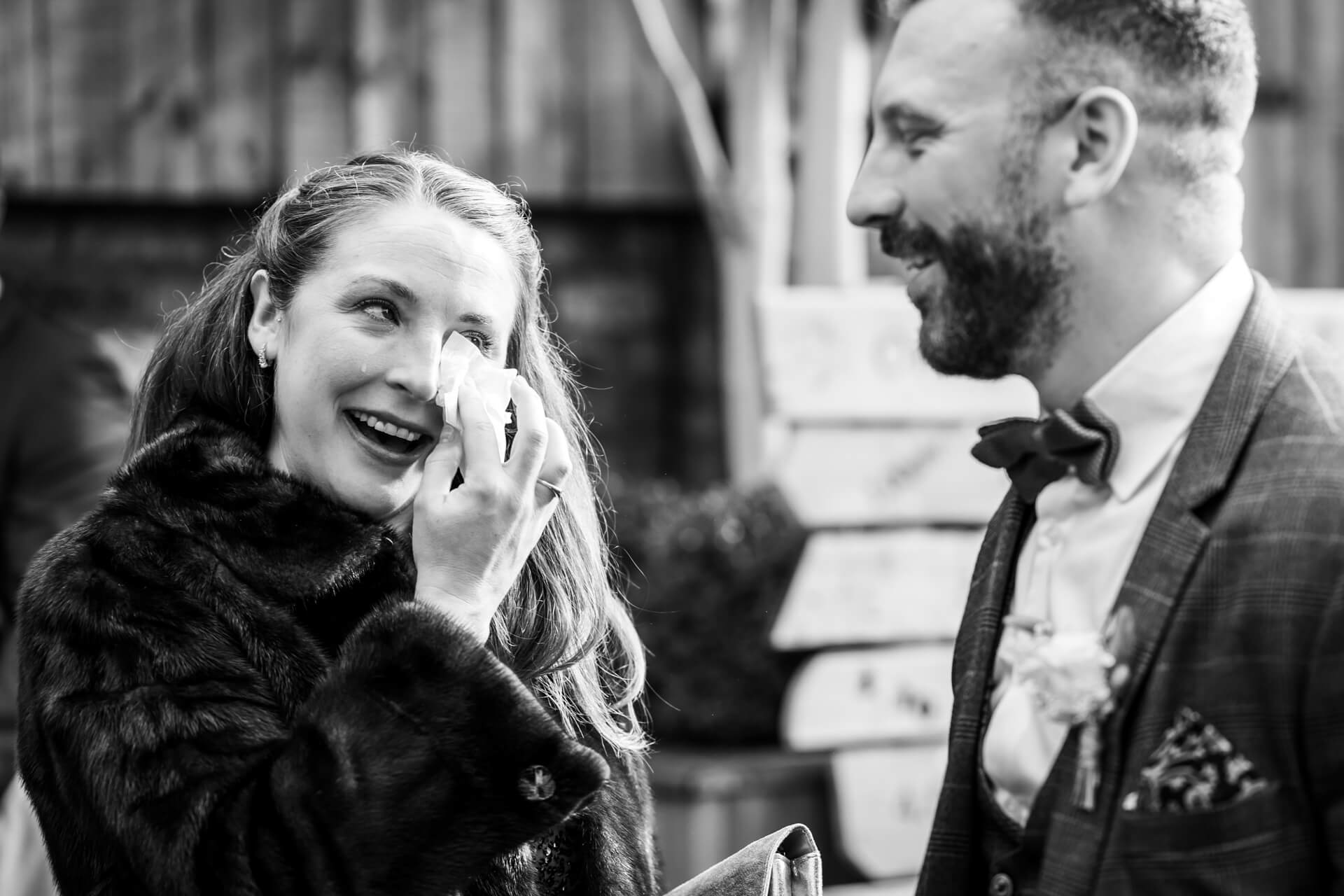 Woman wiping tears, smiling at groom at a wedding