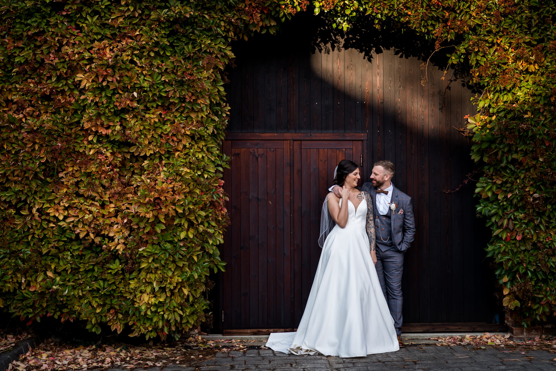 Couple in elegant wedding attire smiling by rustic doorway at The Normans wedding barn