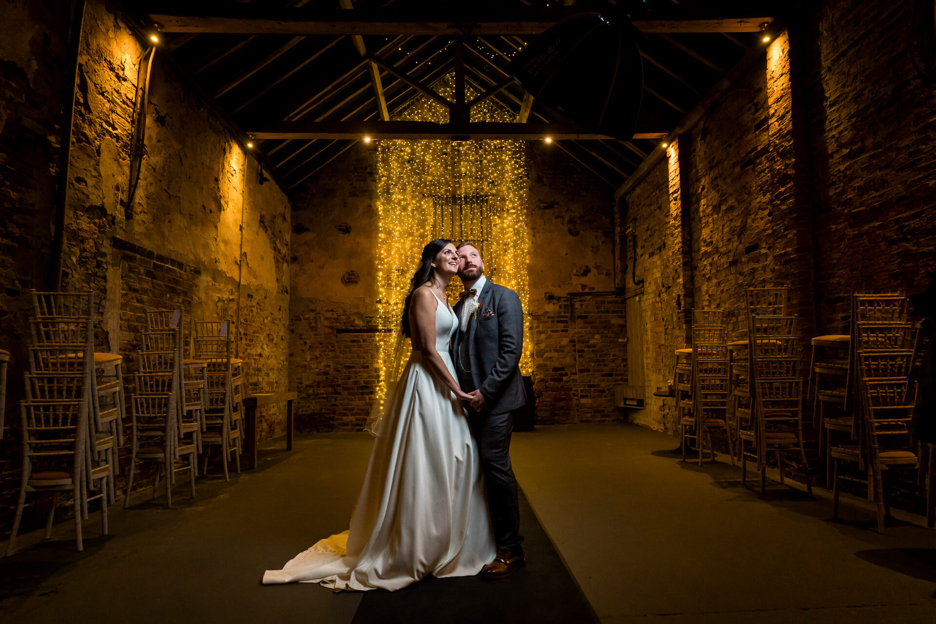 Bride and groom embracing in rustic lit venue at The Normans wedding barn