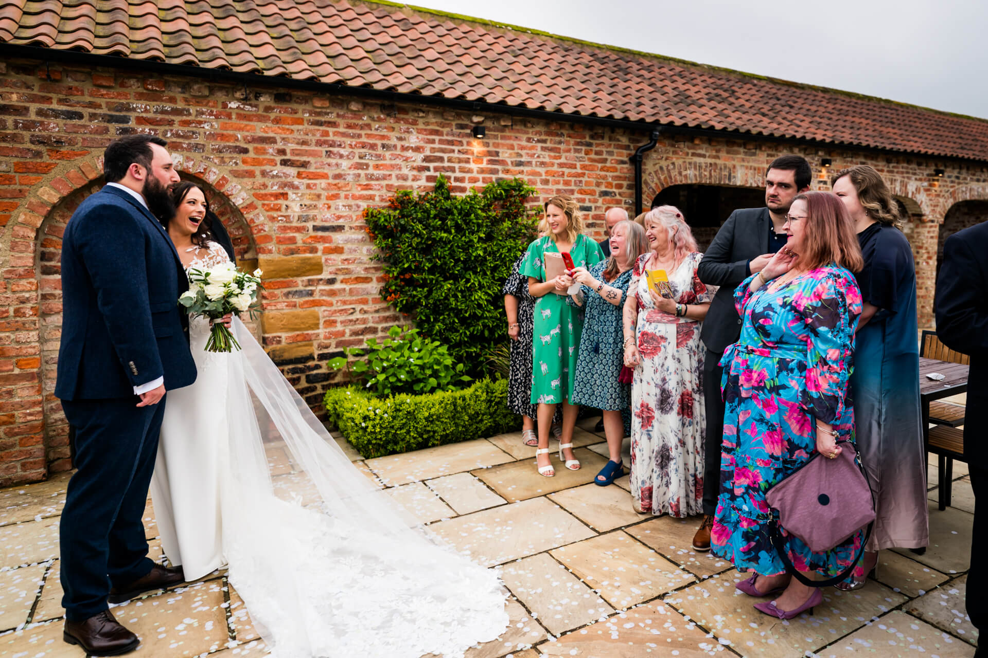 Newlyweds laughing with guests at outdoor wedding.