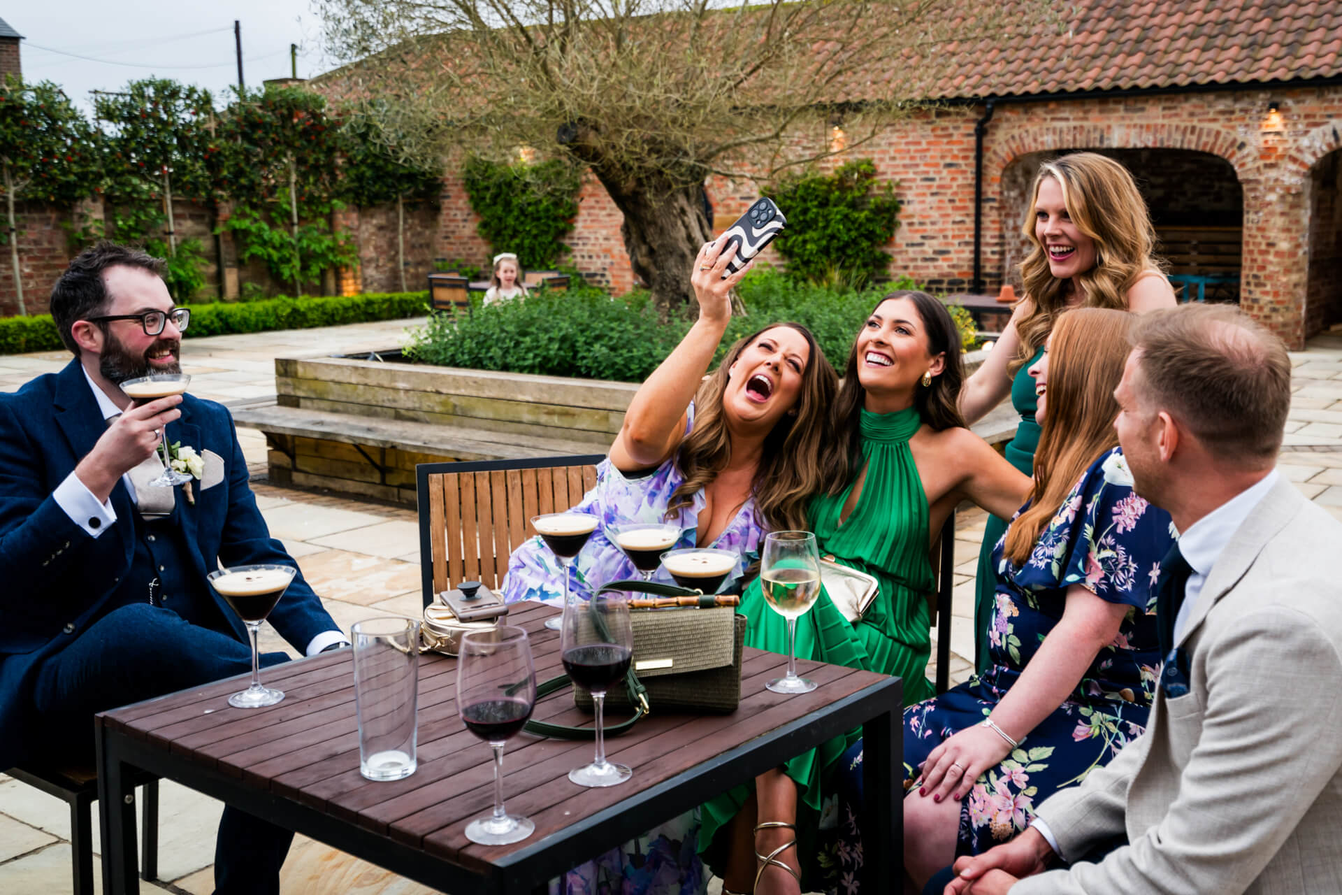 Friends enjoying drinks and selfies at outdoor wedding reception
