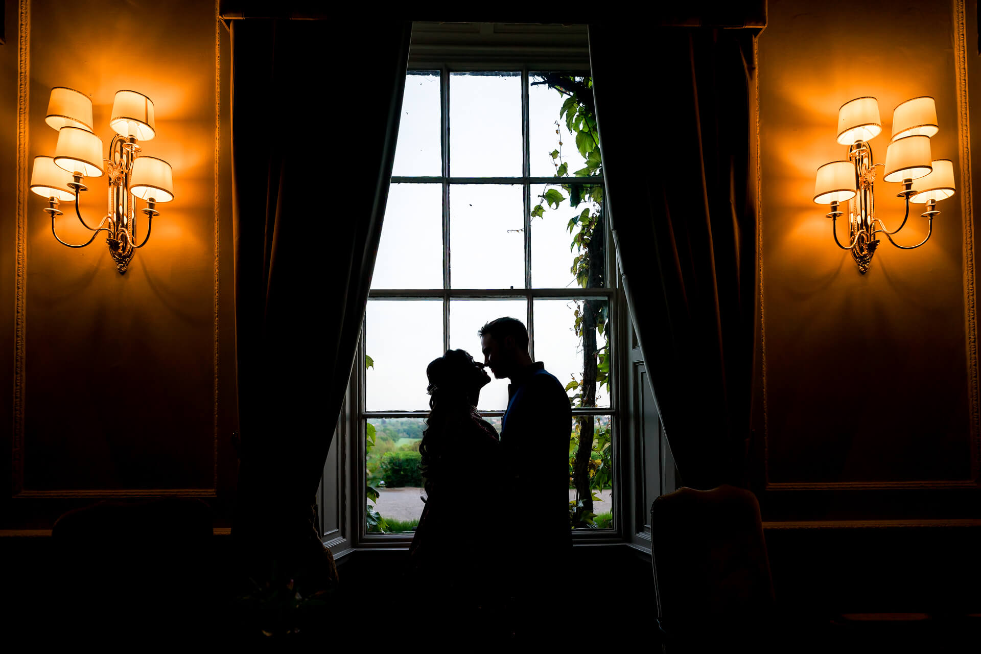 Silhouetted couple kissing by window with ornate lamps at Woodall hotel