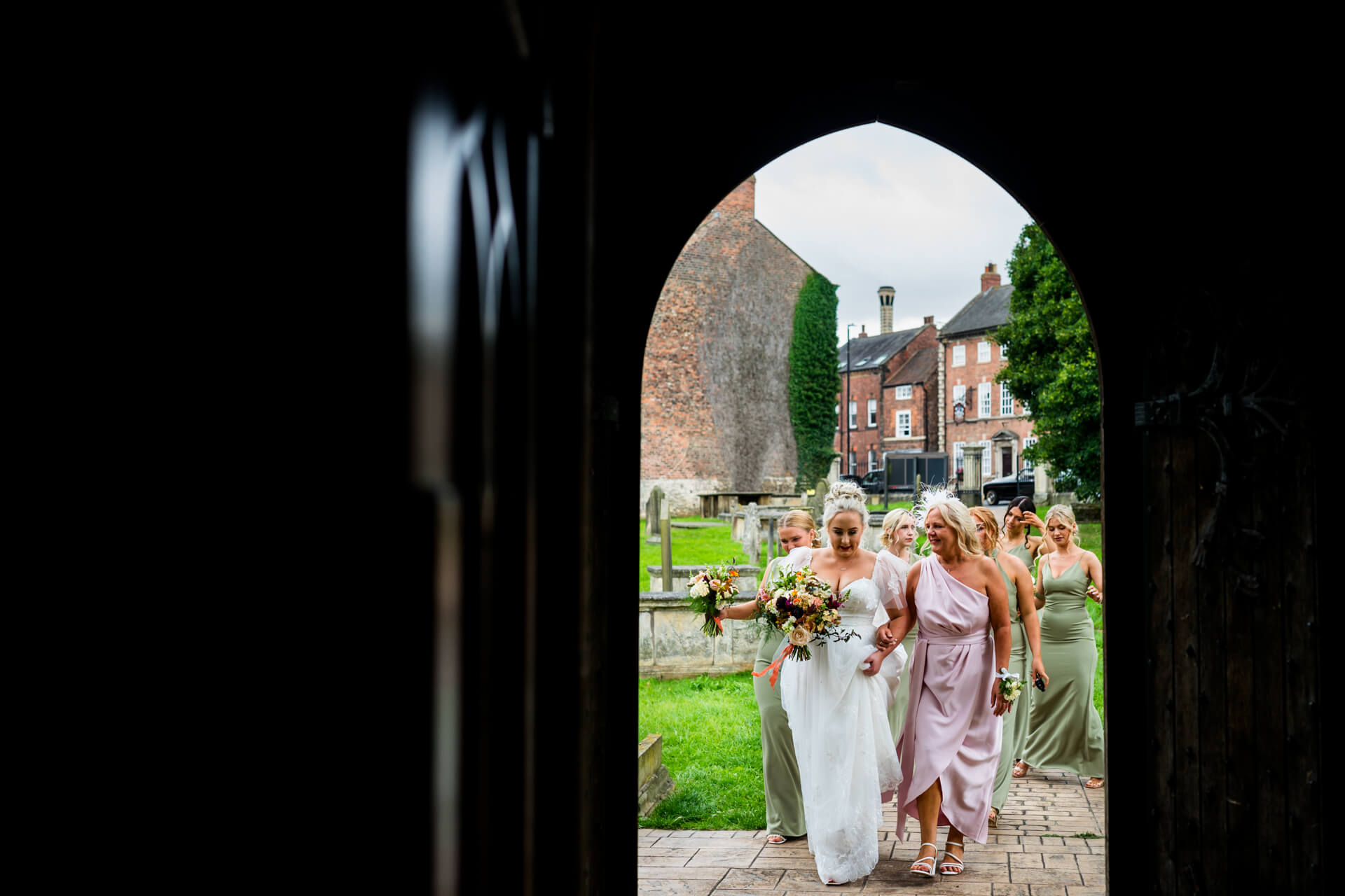 Bride walking with bridal party at village church entrance