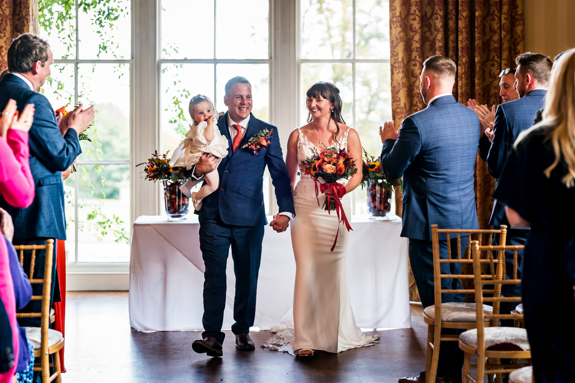 Wedding couple with child applauded by guests indoors