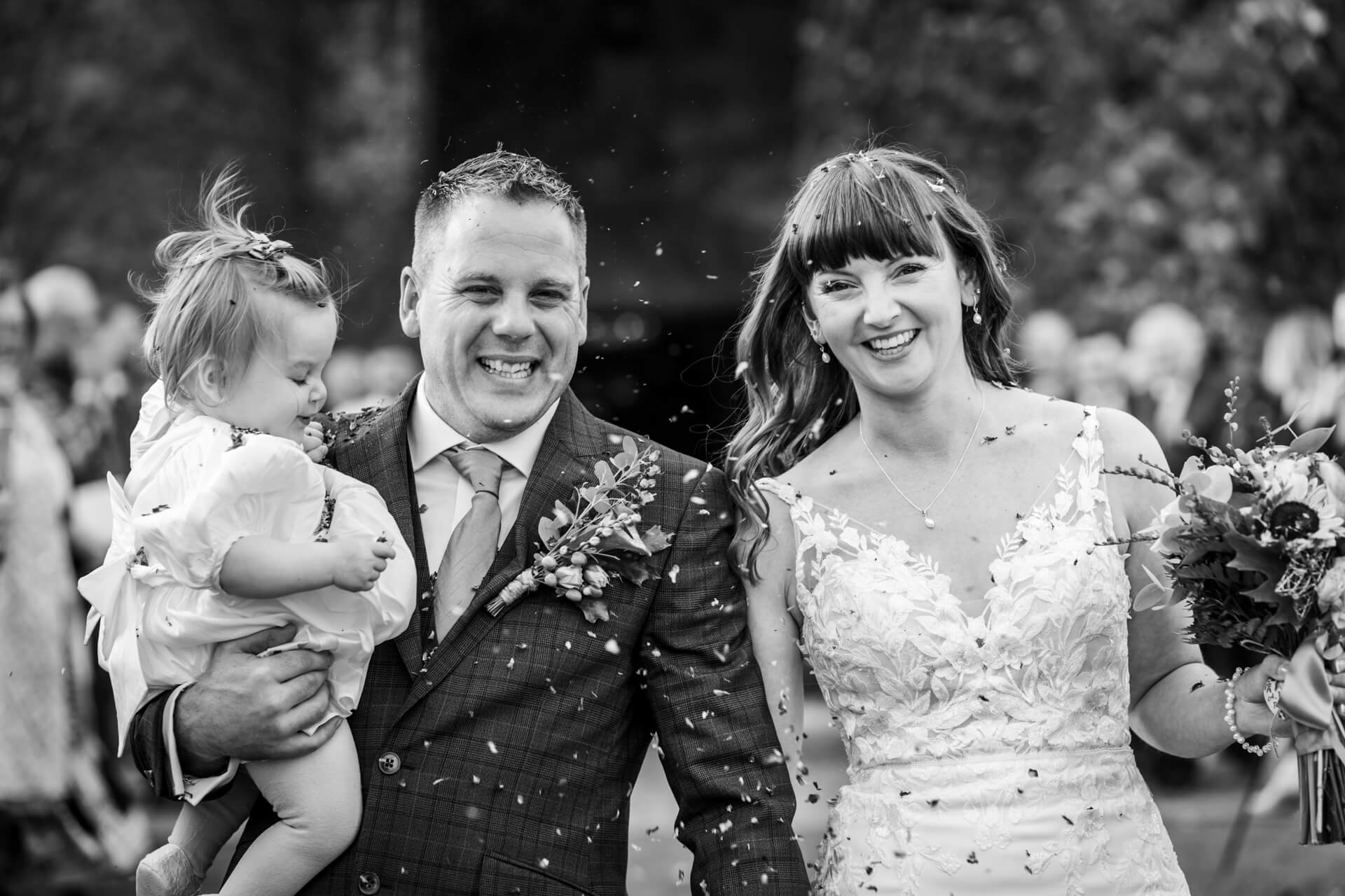 Joyful wedding couple with toddler during confetti toss