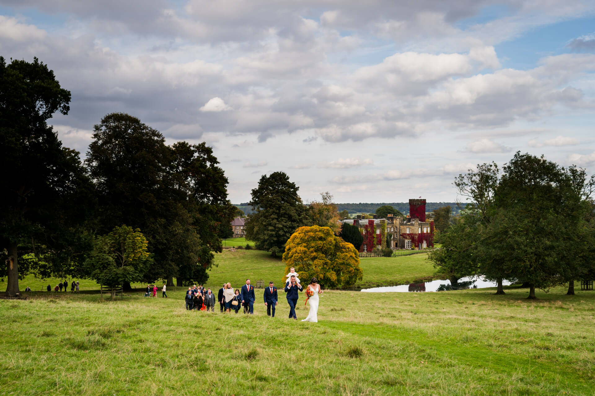 Wedding party walking in scenic Swinton Park estate with historic building
