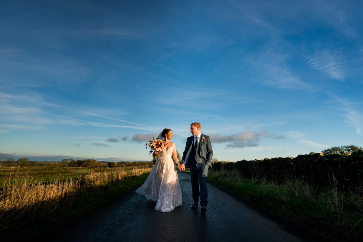 Bride and groom walking on country road at sunset