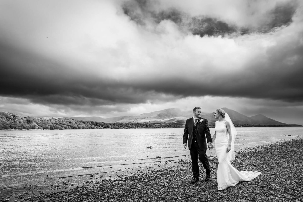 Bride and groom strolling by dramatic lake in monochrome