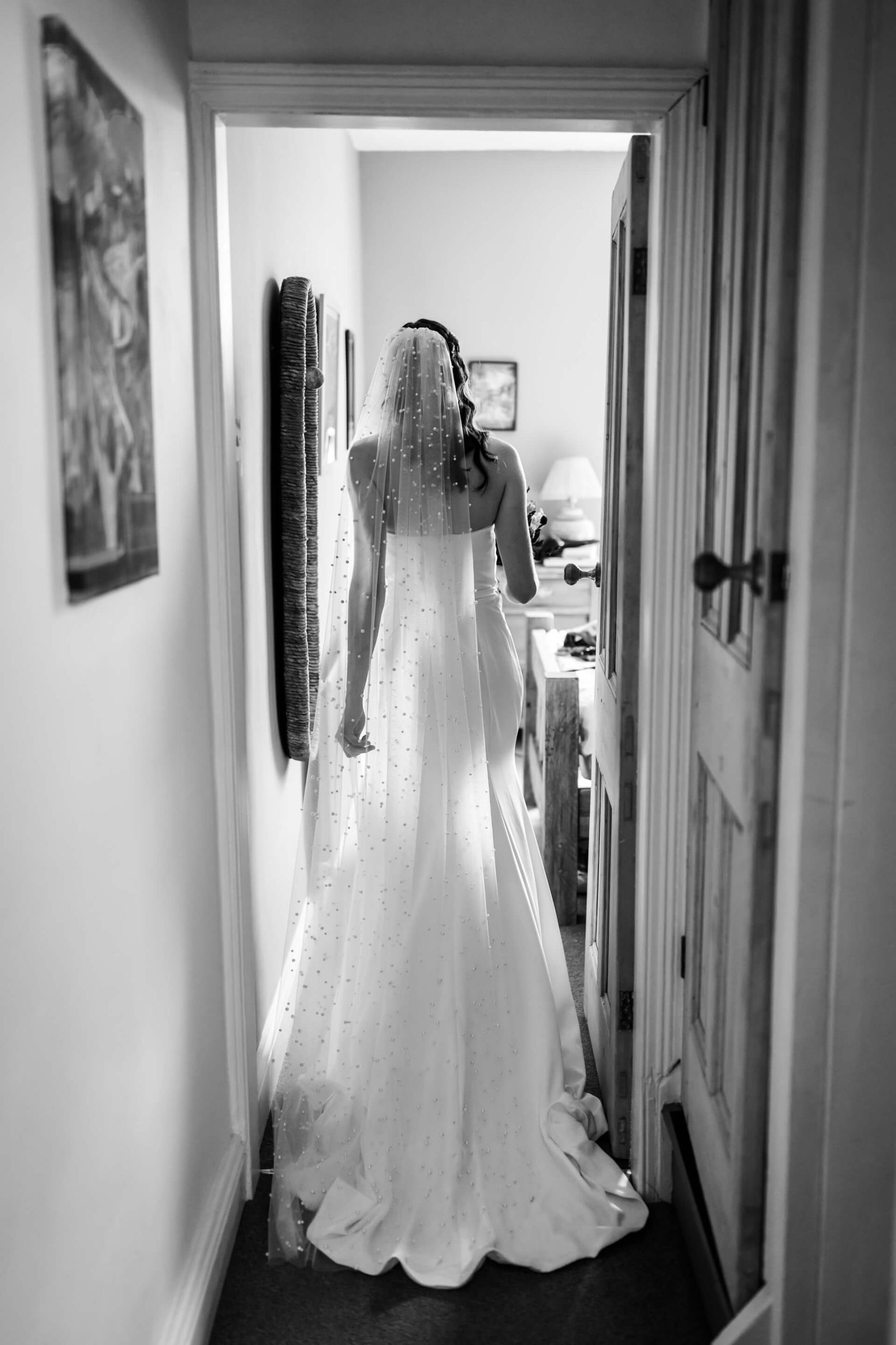 Bride in white dress entering room, black and white photo