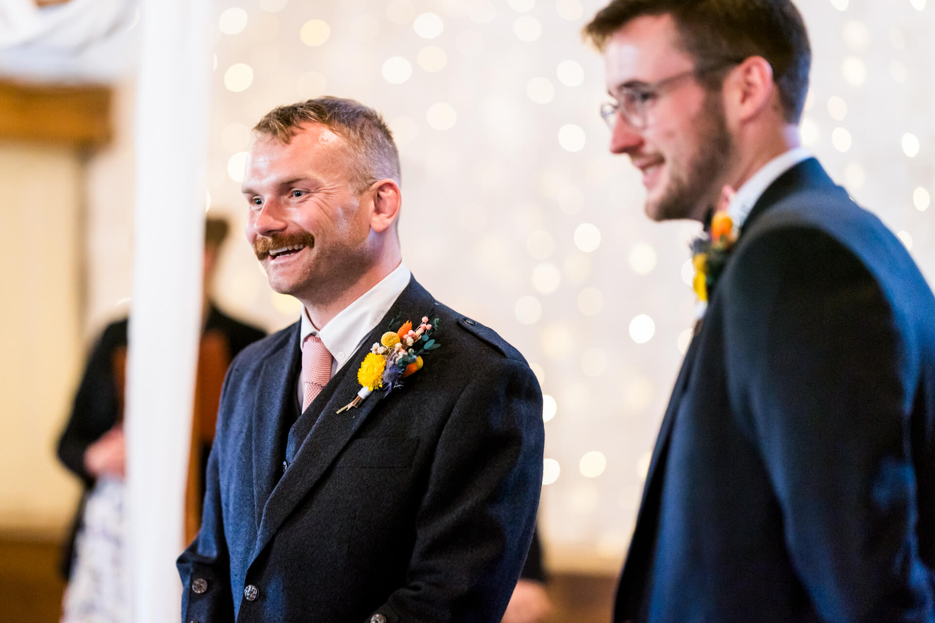Two groomsmen smiling at wedding, one with floral boutonniere