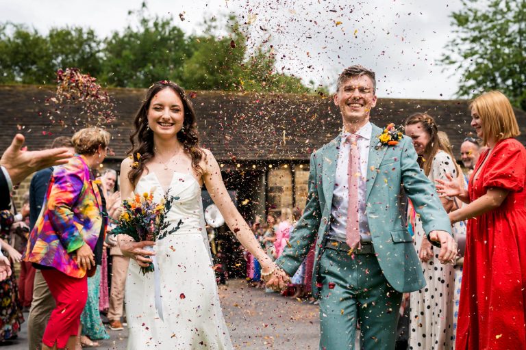 Newlyweds smiling, walking under shower of flower petals.