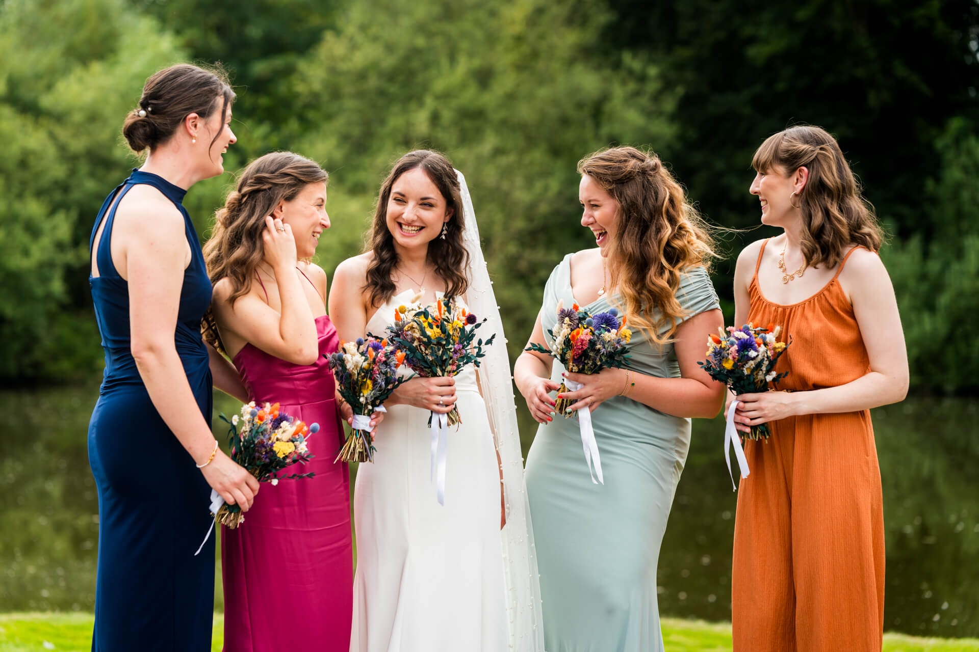 Bride and bridesmaids laughing outdoors with bouquets