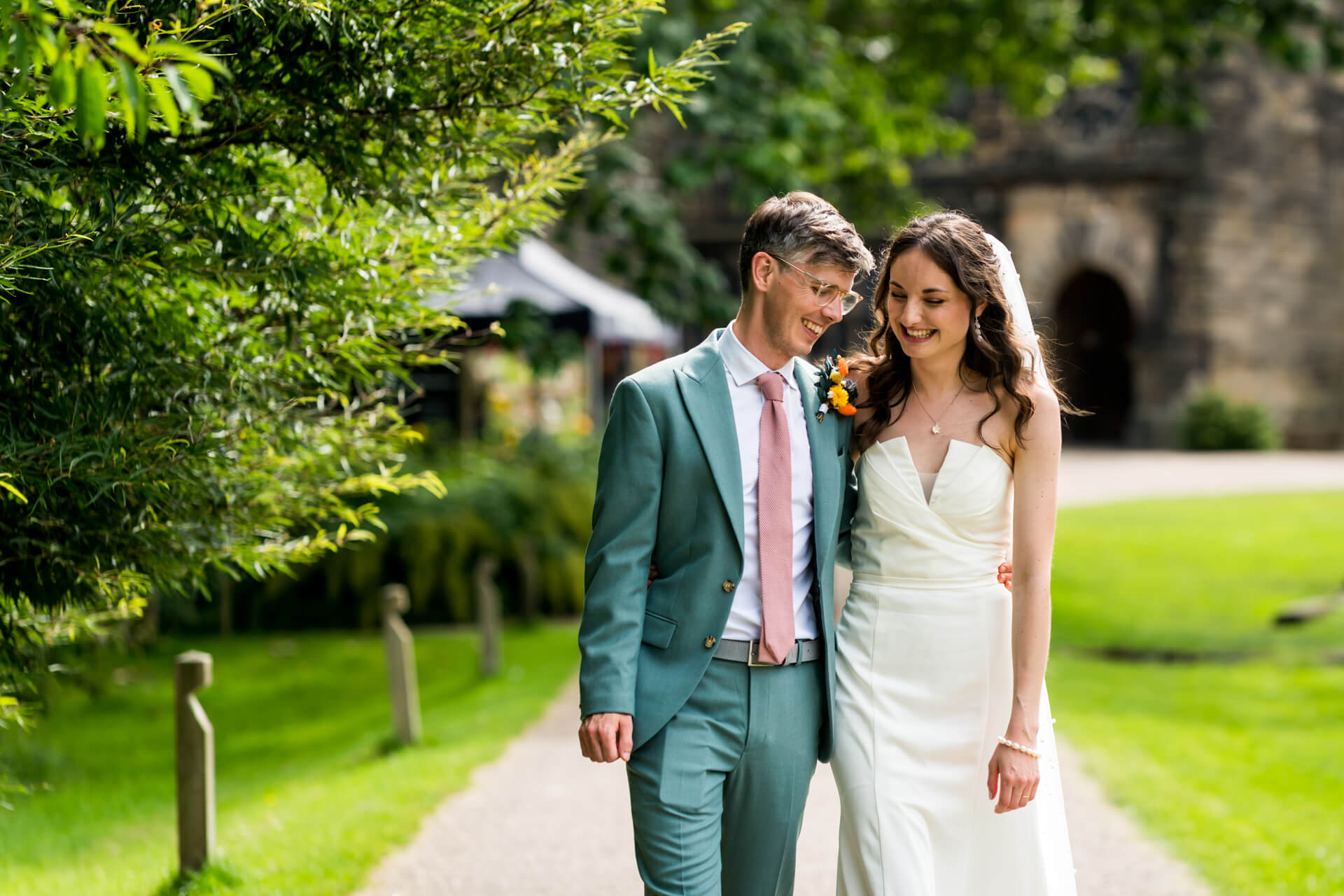 Newlyweds walk smiling in lush garden at East Riddlesden Hall