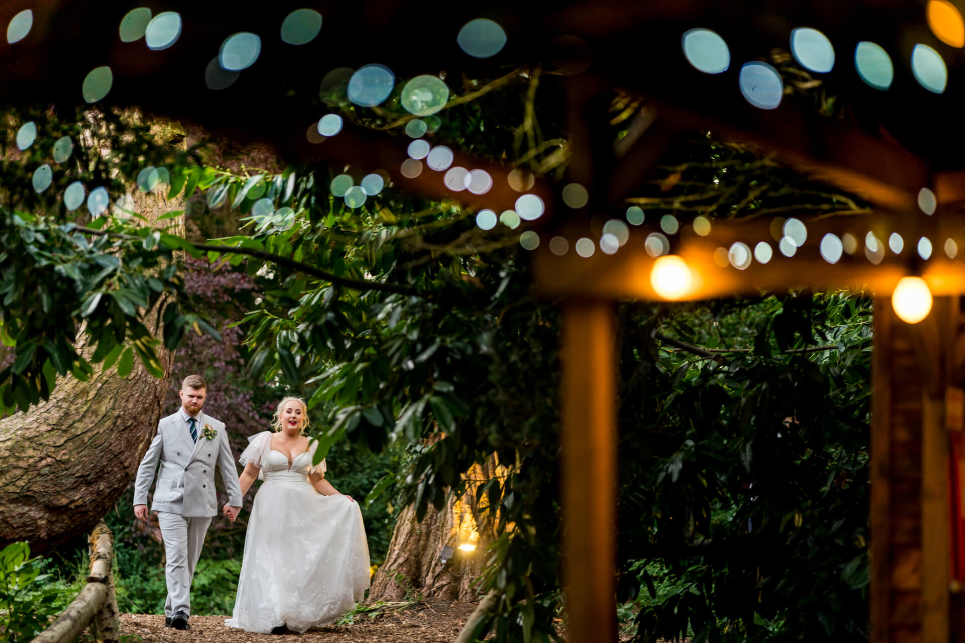 Couple walking in forest at Hazlewood Castle, wedding attire, fairy lights