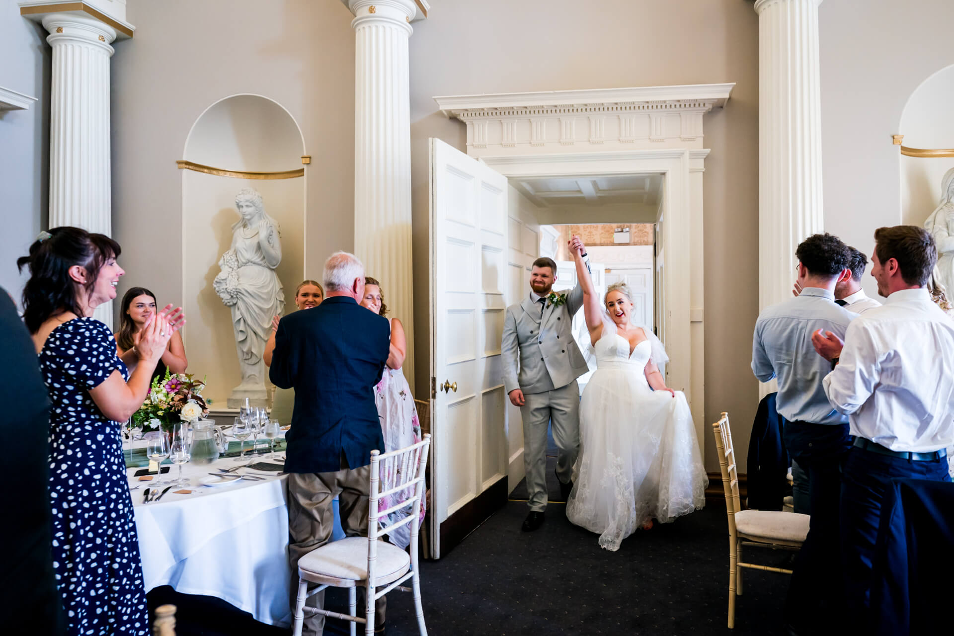 Newlyweds entering wedding reception at Hazlewood Castle amidst applauding guests