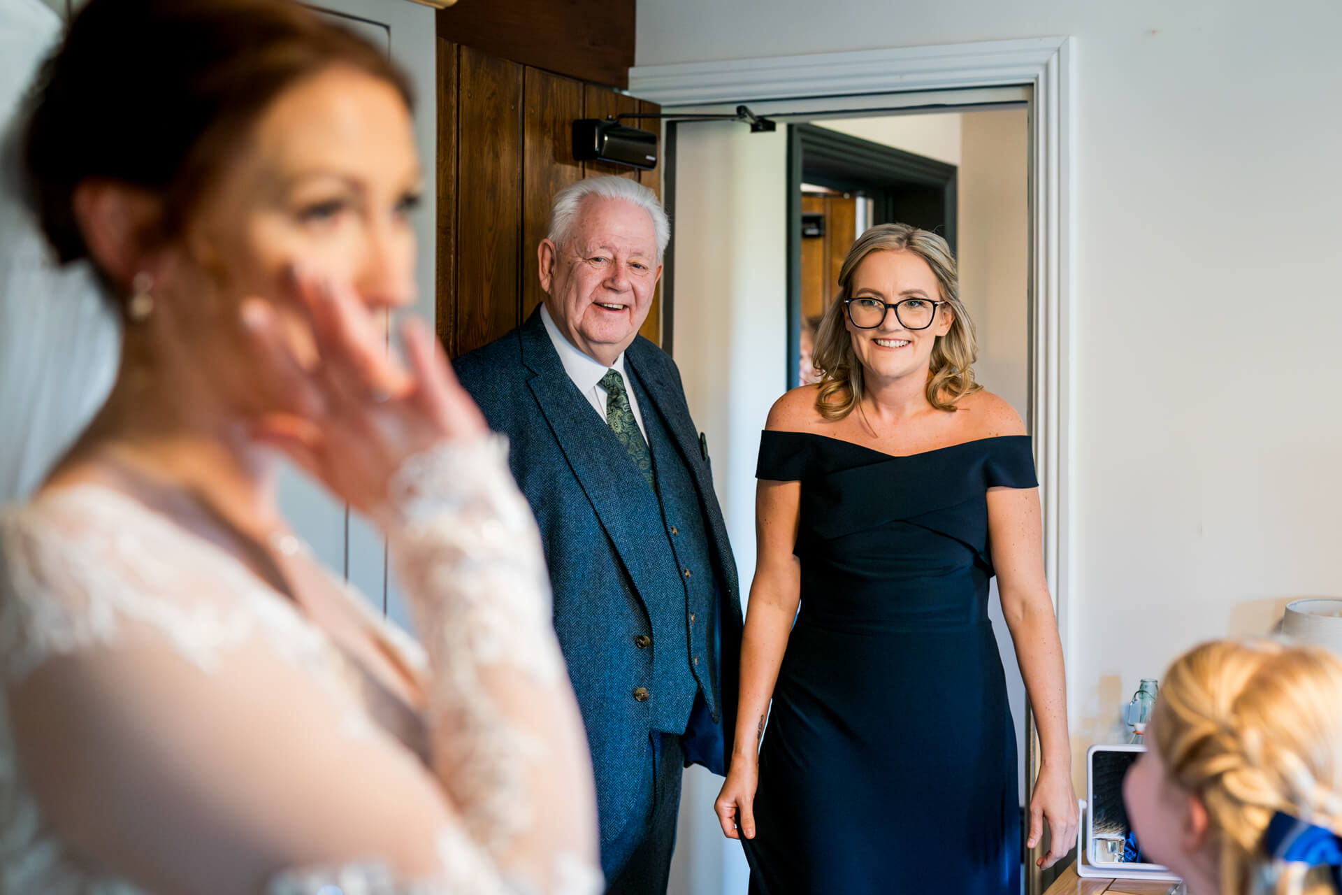 Bride wiping tear, man and woman smiling in room