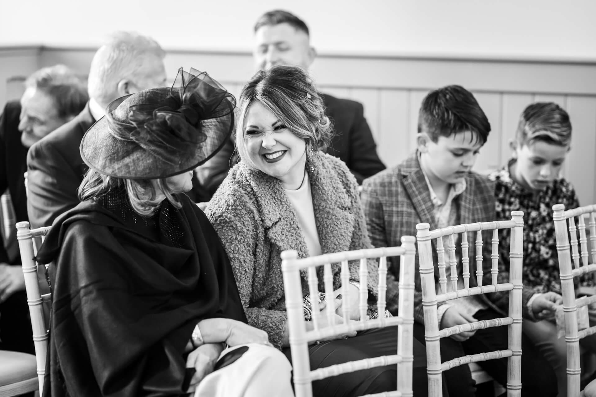Women smiling at joyful wedding ceremony with guests in hats