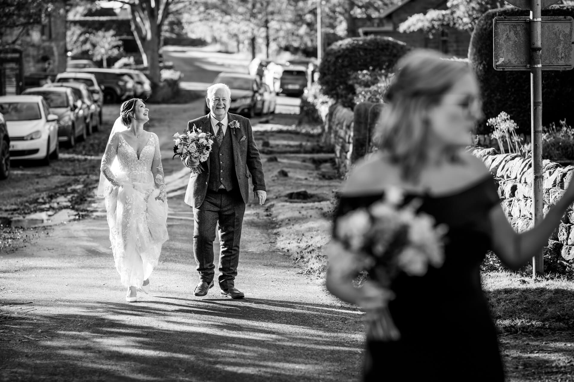 Bride and father walking joyfully along country lane by the Timble Inn