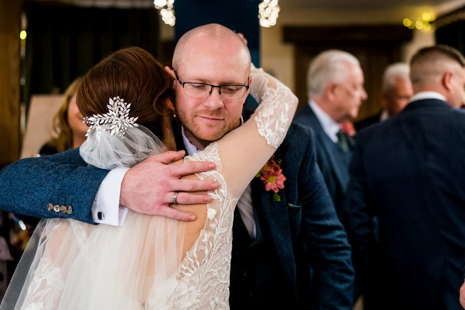 Bride and groomsman embracing warmly at wedding reception.