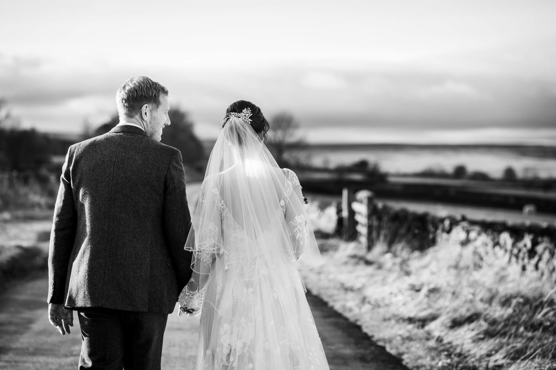 Bride and groom walking on countryside road, black and white