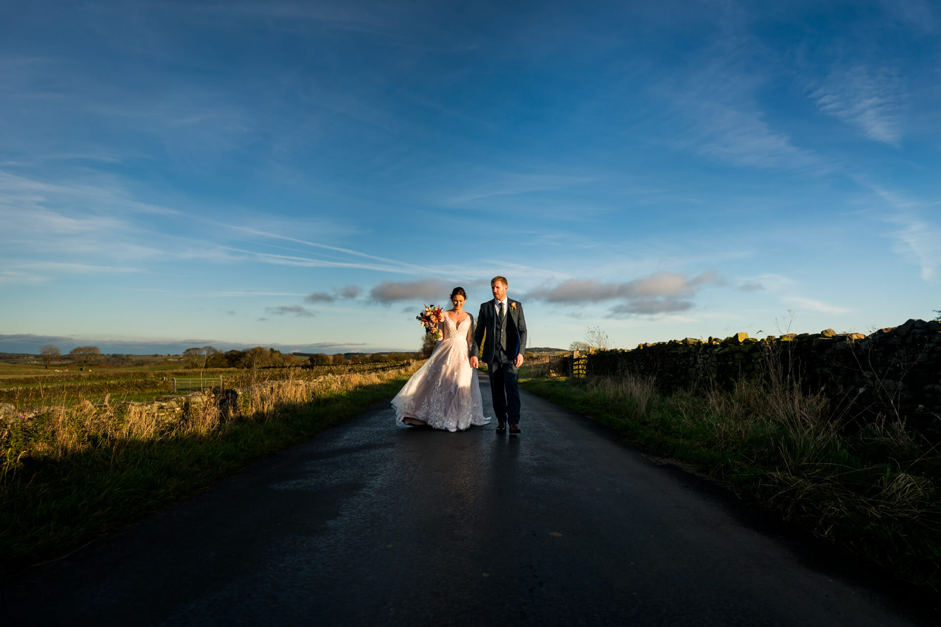 Newlyweds walking on countryside road at sunset