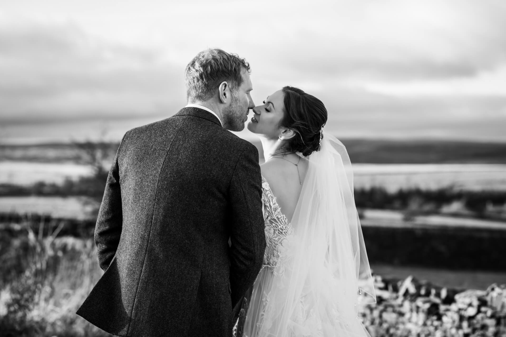 Black-and-white photo of couple kissing on hillside