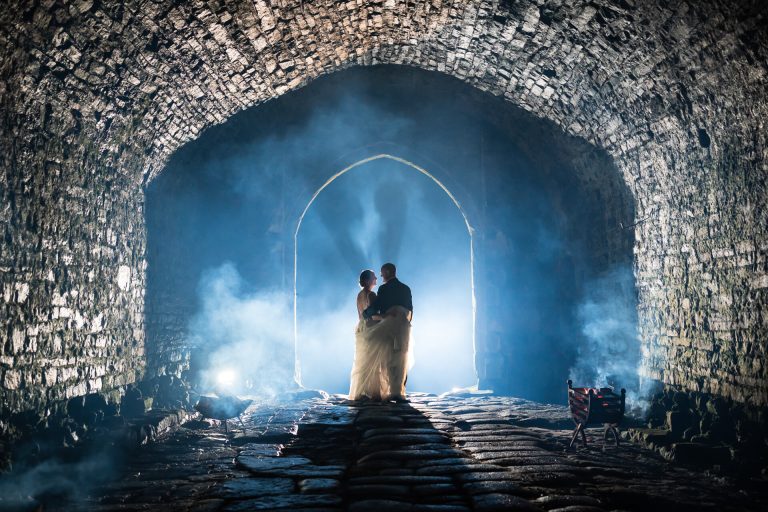 Wedding couple embracing in misty, ancient stone archway at Bolton Castle