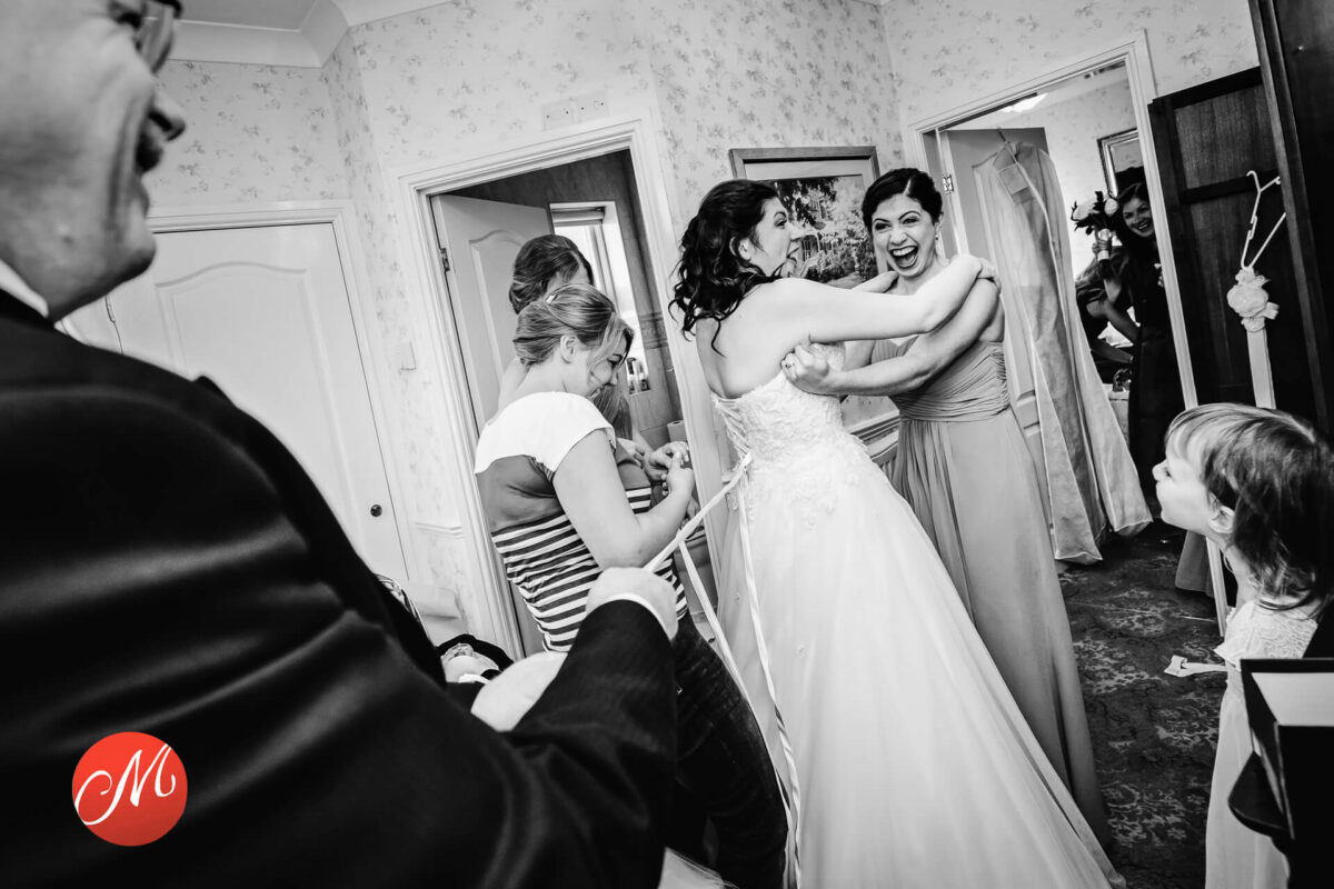 Bridal party helping bride with dress preparation.