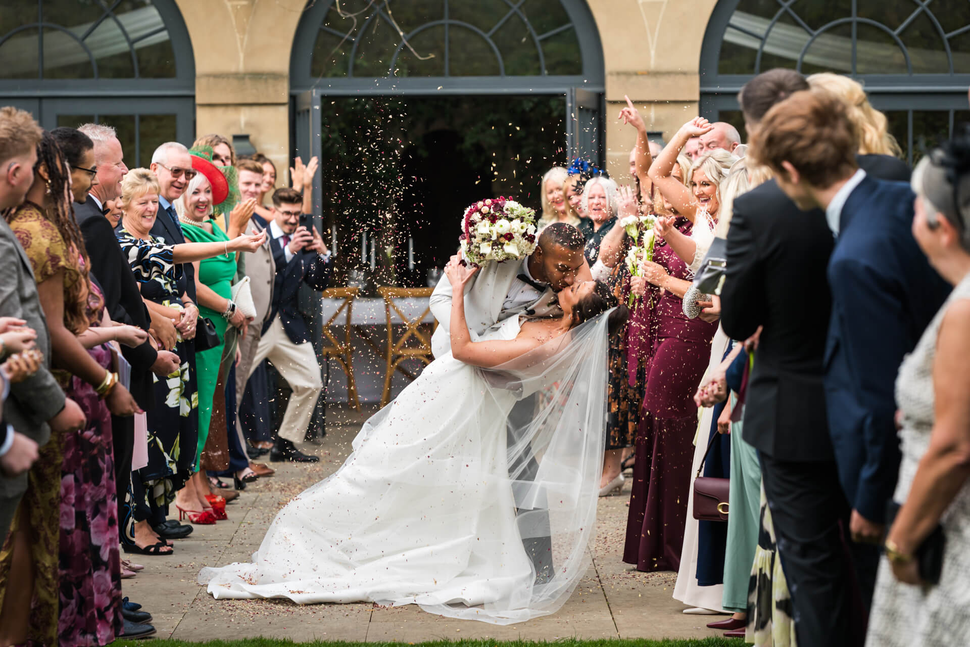 Bride and groom kiss surrounded by cheering guests.