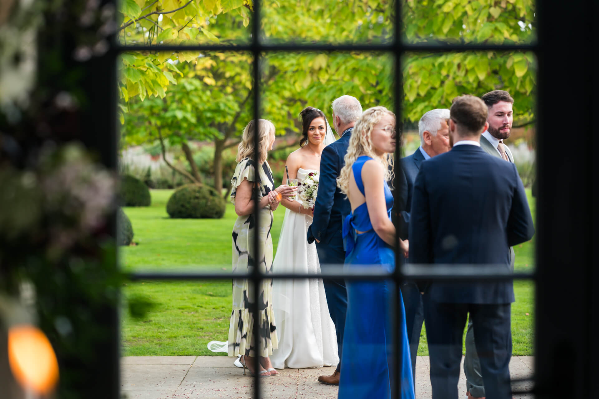 Group gathered outside in garden setting, framed by window.