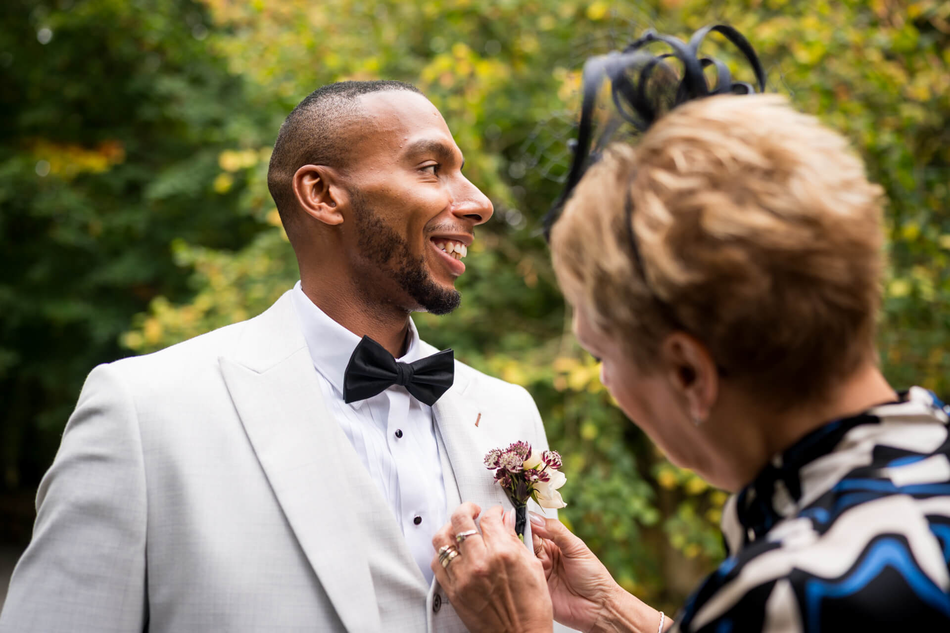 Smiling groom getting boutonniere adjusted outdoors